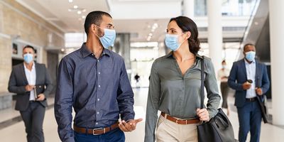 Two business people walking and talking while wearing masks indoors