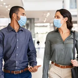 Two business people walking and talking while wearing masks indoors