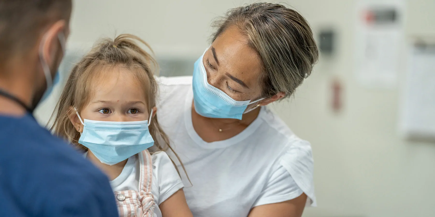 Mother with young child at doctors office, wearing masks