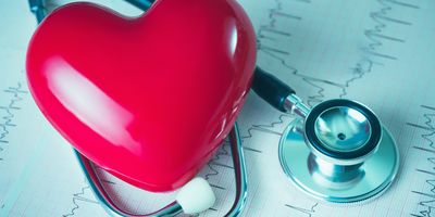 A plastic hear lying next to a stethoscope and a heart rate read out