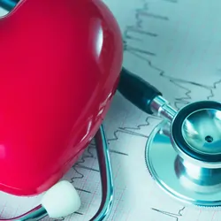 A plastic hear lying next to a stethoscope and a heart rate read out