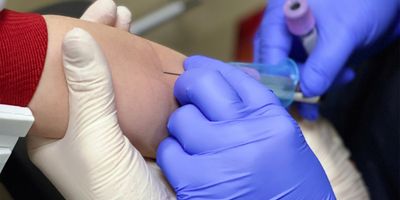 Health care professional drawing blood from the arm of a young patient