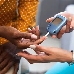 Female health care provider takes blood glucose sample of a Black patient