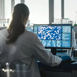 Photo of a clinical lab professional sitting at a computer designing a precision medicine lab.
