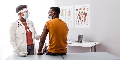 Doctor wearing mask speaks with patient in examination room