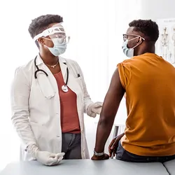 Doctor wearing mask speaks with patient in examination room