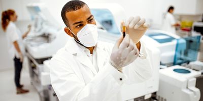 Researcher wearing a mask, holding a vial of blood for study