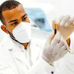 Researcher wearing a mask, holding a vial of blood for study