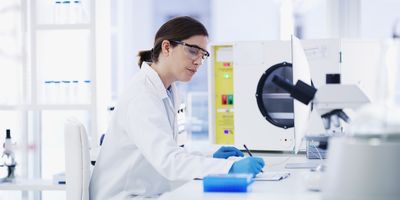 Photo of a clinical lab professional wearing a lab coat and gloves in an automated lab.