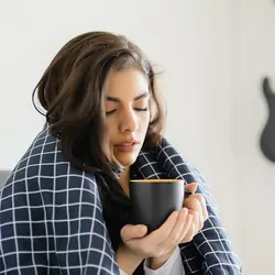 Woman, sick in bed with a mug of tea