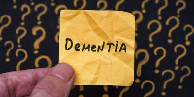 A man holding a yellow piece of paper with the word dementia on it in his hand