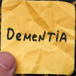 A man holding a yellow piece of paper with the word dementia on it in his hand