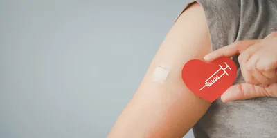 Person with band aid on arm where they just got vaccinated holding a cut out heart with a syringe on it