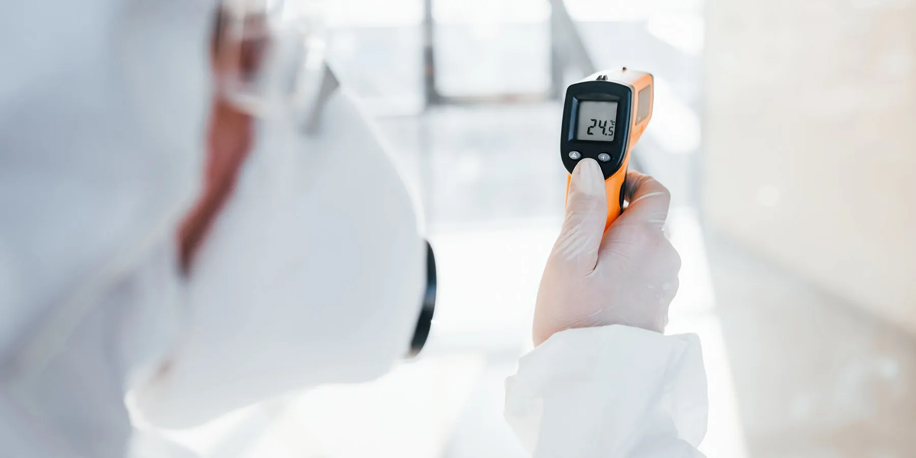 Photo of a clinical lab professional wearing PPE and a using a temperature monitoring device.