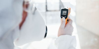 Photo of a clinical lab professional wearing PPE and a using a temperature monitoring device.