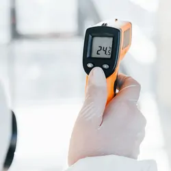 Photo of a clinical lab professional wearing PPE and a using a temperature monitoring device.