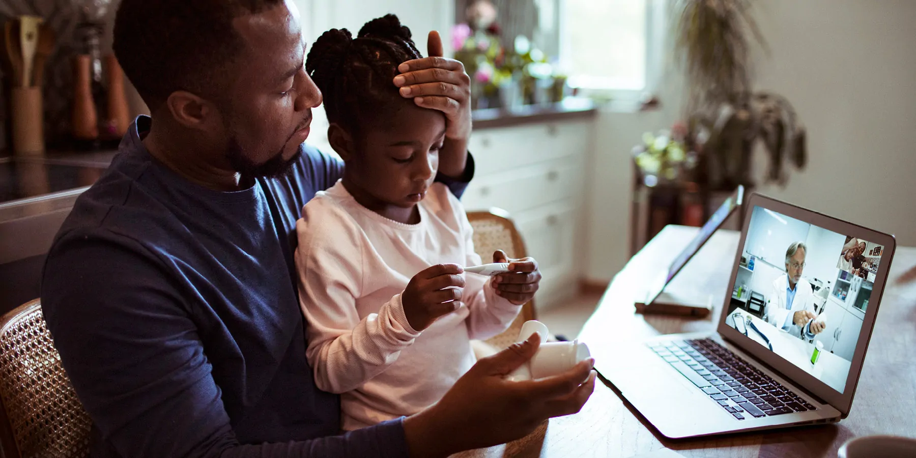 What Is Needed to Ensure Telemedicine Is Truly Equitable? Photo of a Black man taking his daughter's temperature while on a telehealth call with a doctor.