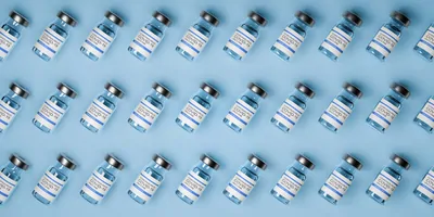 Photo of glass vials of COVID-19 vaccines against a blue background.