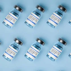Photo of glass vials of COVID-19 vaccines against a blue background.