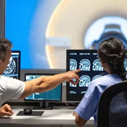 Rear view of male and female MRI technologist sitting at the console in the operating room 