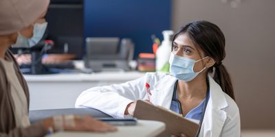 A female doctor bend's down to eye level as she talks with a cancer patient