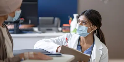 A female doctor bend's down to eye level as she talks with a cancer patient