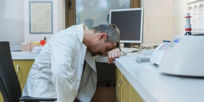 Photo of a burned out clinical lab professional resting their head on their lab desk.
