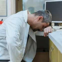 Photo of a burned out clinical lab professional resting their head on their lab desk.