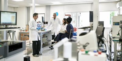 Photograph showing a group of four clinical lab personnel having an informal meeting in the lab space to discuss protocols and reagents for standardizing flow cytometry.