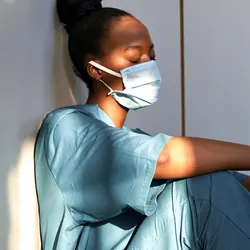 Tired exhausted scrub nurse wears face mask blue uniform gloves sits on hospital floor