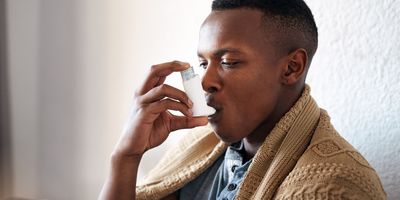 Photograph of a Black youth using an inhaler to manage his asthma attack.