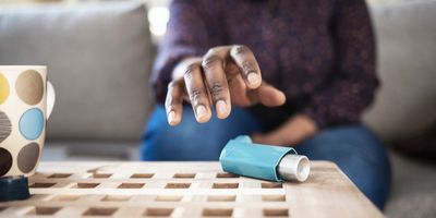 Woman suffering asthma attack reaching inhaler sitting on a couch in the living room