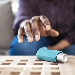 Woman suffering asthma attack reaching inhaler sitting on a couch in the living room