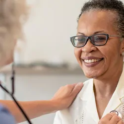 A senior black women is having her heart checked by a female doctor