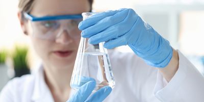 Photograph of clinical lab professional examining a beaker of purified water.