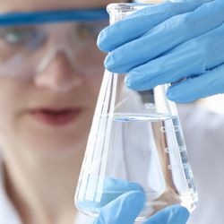 Photograph of clinical lab professional examining a beaker of purified water.
