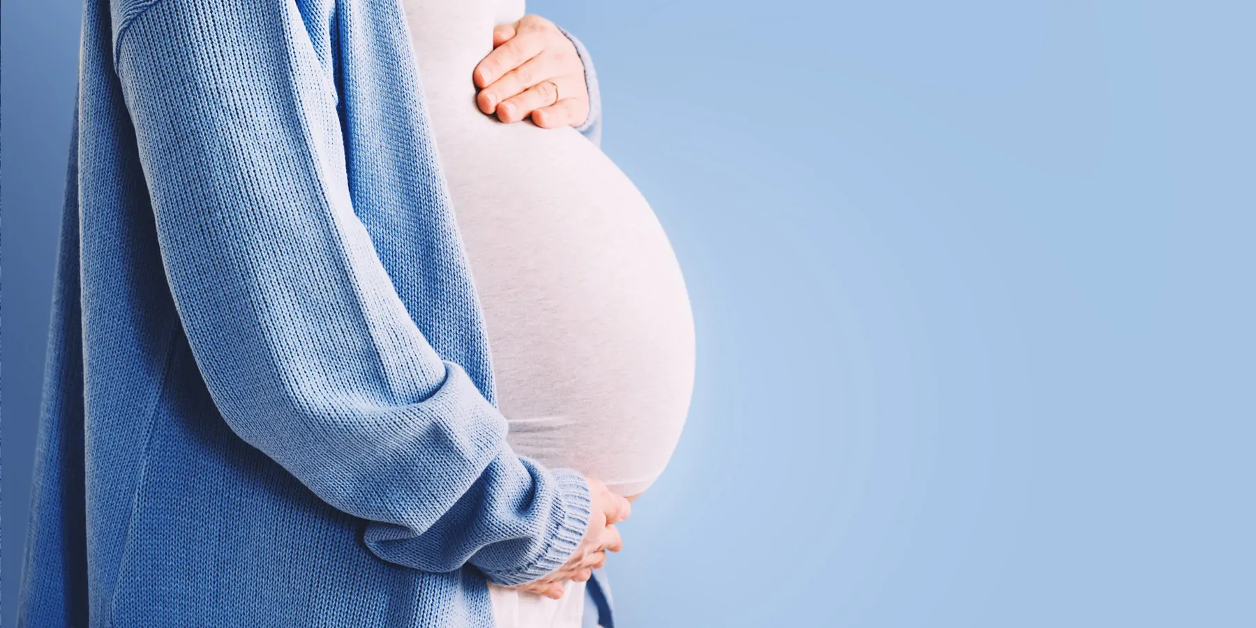 Pregnant woman hugging her belly on blue background