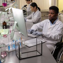 Photo of a Black clinical laboratory scientist using a wheelchair in an accessible clinical lab.