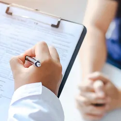 Close-up of a male doctor hand hold a silver pen and showing pad in hospital
