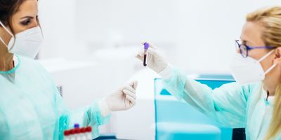 Photograph of two clinical lab personnel holding up a test tube of blood while performing analysis in a hematology lab.