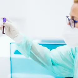 Photograph of two clinical lab personnel holding up a test tube of blood while performing analysis in a hematology lab.