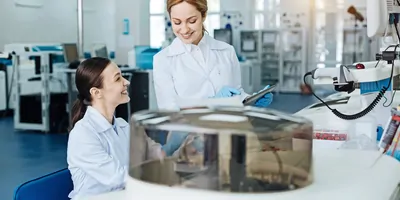 Photograph of two clinical lab personnel discussing and monitoring the flow cytometry workflow on their handheld tablet device.