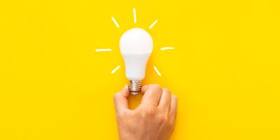 Photograph of a hand holding a bulb on a yellow background to represent sustainability.