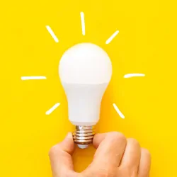 Photograph of a hand holding a bulb on a yellow background to represent sustainability.
