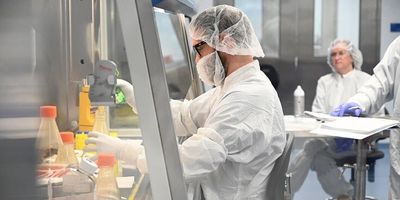 Photo of a clinical professional wearing PPE sitting at a biological safety cabinet preparing the gene therapy.