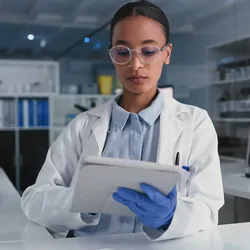 Photo of a Black clinical laboratory professional holding a clinical trial lab manual in a laboratory.