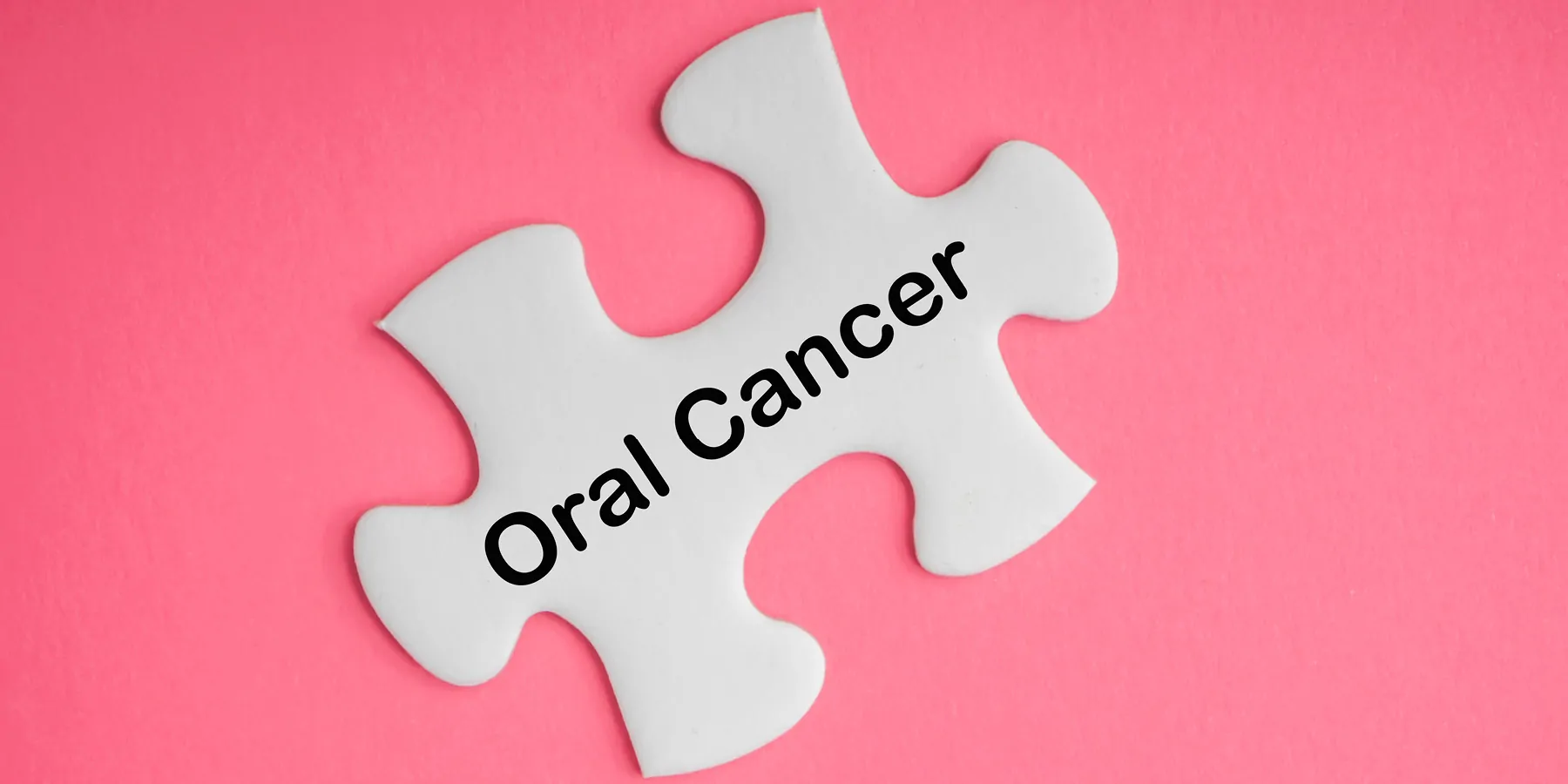 White puzzle piece with the words "Oral Cancer" written on it on a pink background