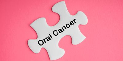 White puzzle piece with the words "Oral Cancer" written on it on a pink background