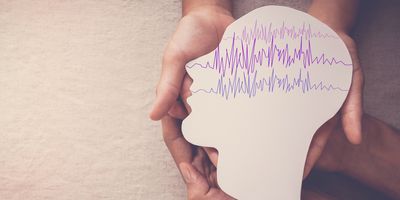 Hands holding a paper cut out of a human head with brain waves traced on it