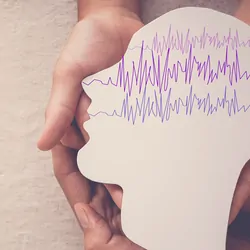 Hands holding a paper cut out of a human head with brain waves traced on it